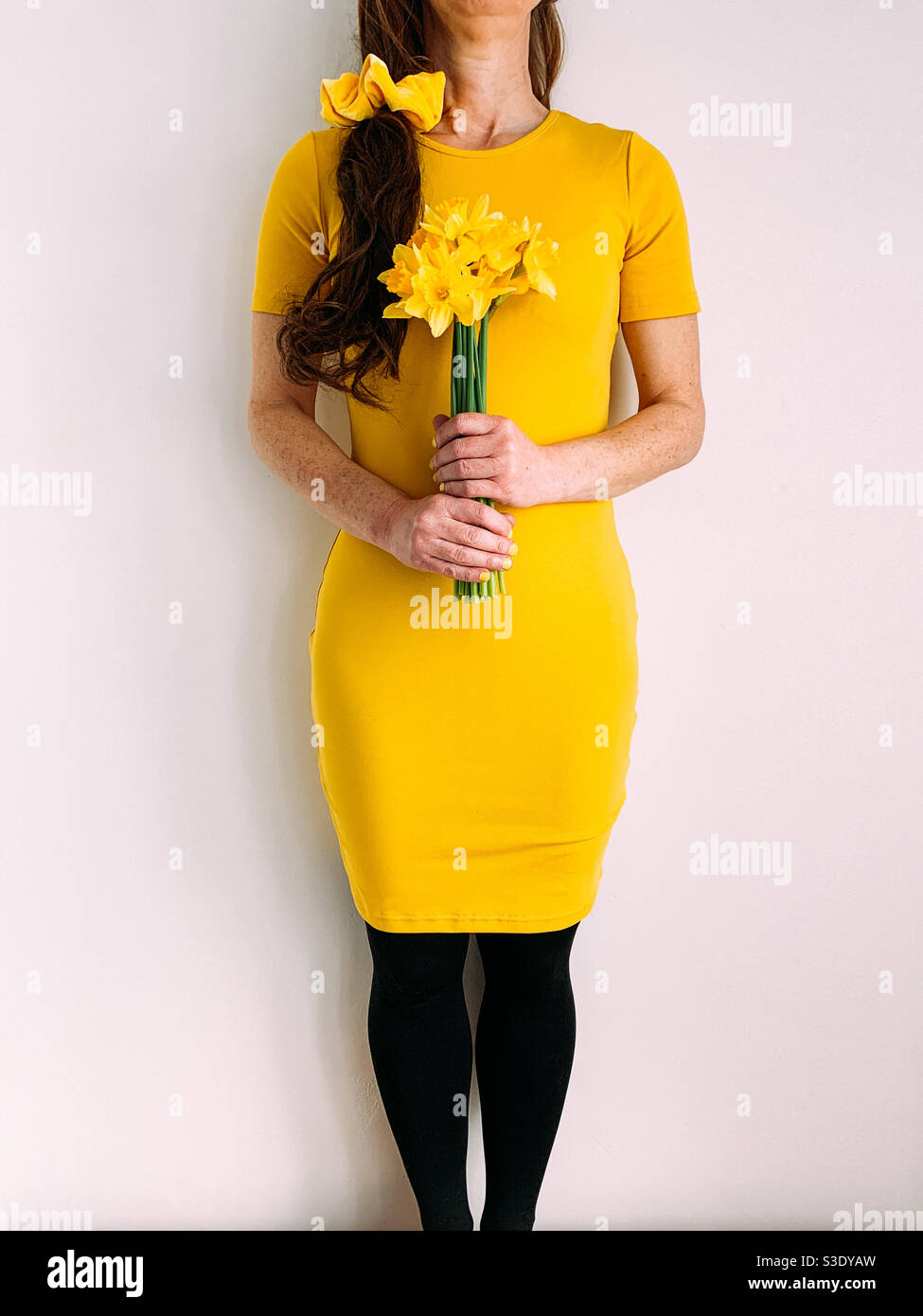 Woman holding a bunch of yellow daffodils wearing a yellow dress Stock Photo