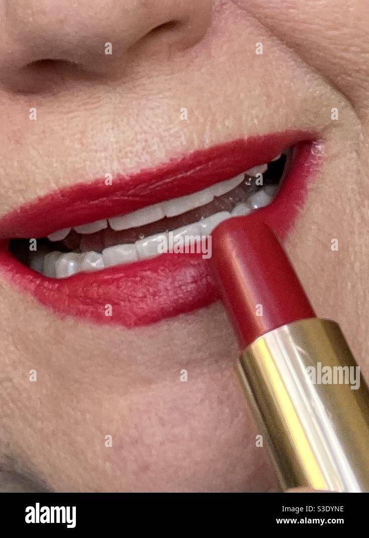 Woman applying lipstick to her partially open mouth showing white teeth - Smartphone Captured Stock Image