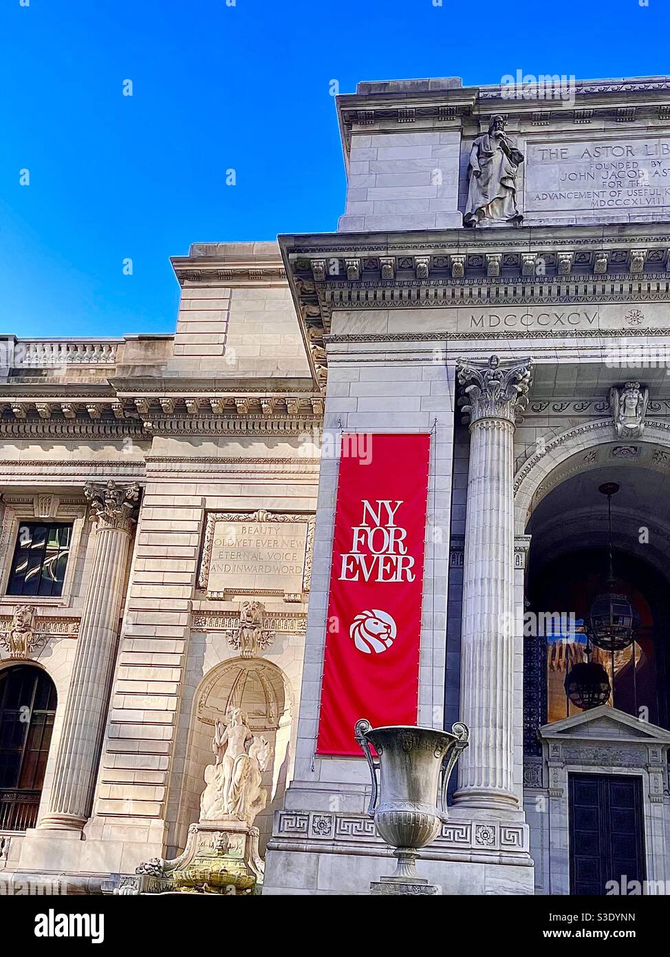 A bright red and white banner sane New York for ever hanging on the stone façade and statuary of the New York public library Against a bright blue clear sky in Manhattan, New York, USA - Smartphone Captured Stock Image