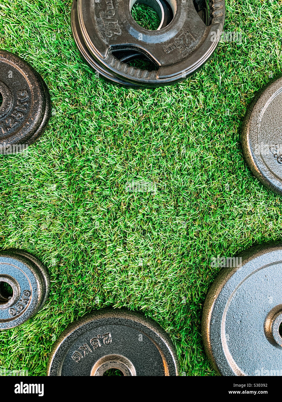 Barbell and dumbbell weight plates on artificial grass - Smartphone Captured Stock Image