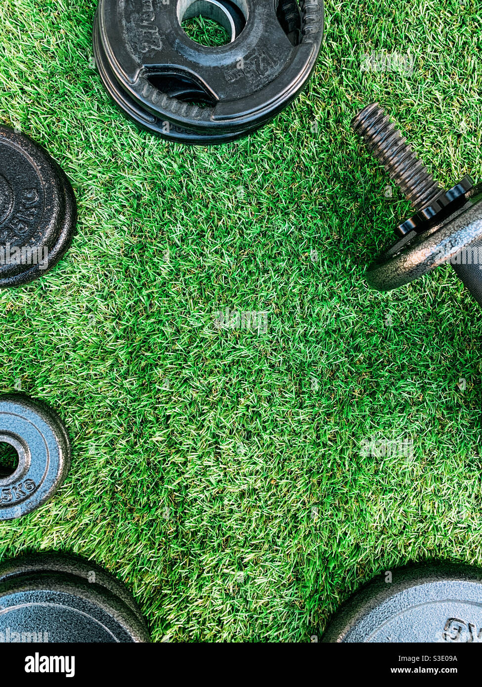 Top view of a set of weight training plates and a dumbbell on artificial grass - Smartphone Captured Stock Image