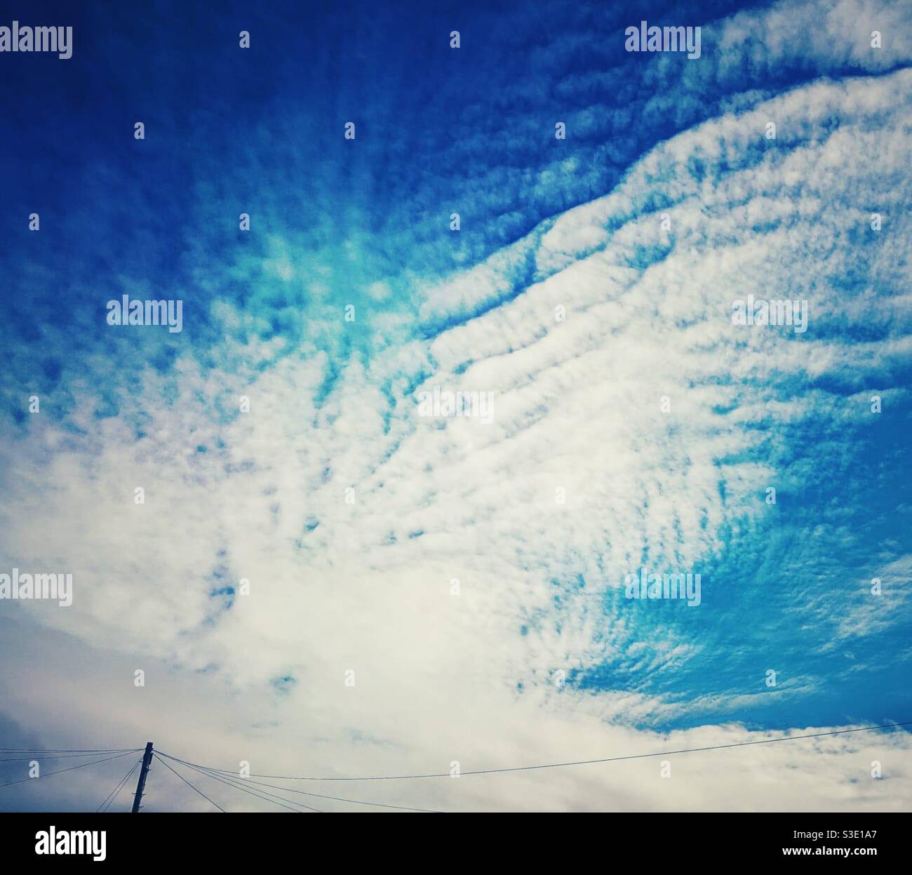 A photograph of a vivid blue sky with wispy clouds and power cables in the corner. Copy space. - Smartphone Captured Stock Image