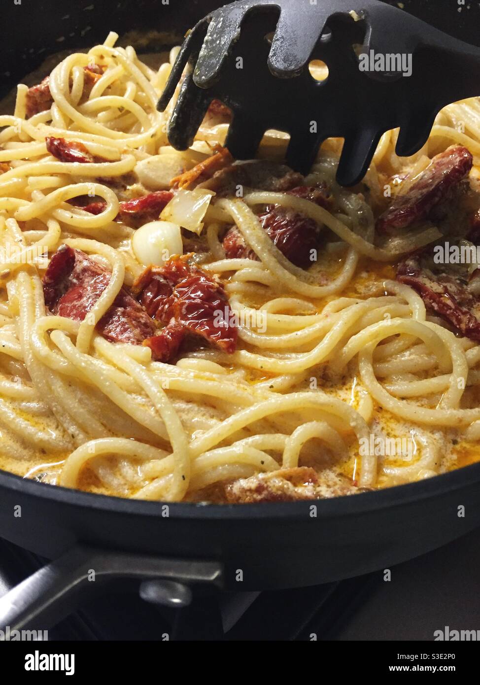 Close up of a pasta fork serving an Italian gourmet entrée of sun-dried tomatoes in a cream sauce on spaghetti noodles - Smartphone Captured Stock Image
