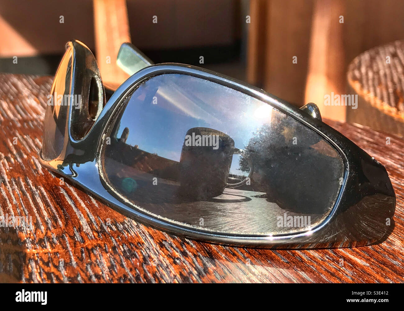 Sunglasses on a wooden table, reflecting a coffee mug, on a sunny summer day. - Smartphone Captured Stock Image