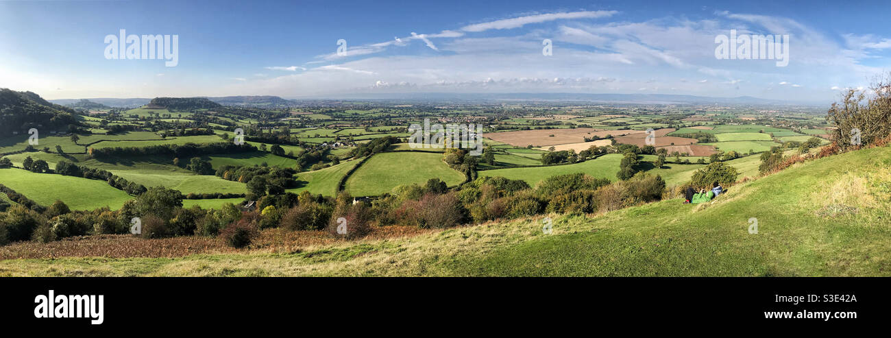 Panorama view from Coaley Peak/Frocester Hill, in the Cotswolds, near Stroud, Gloucestershire, England. Includes two people laying on the grass enjoying the view. Stock Photo