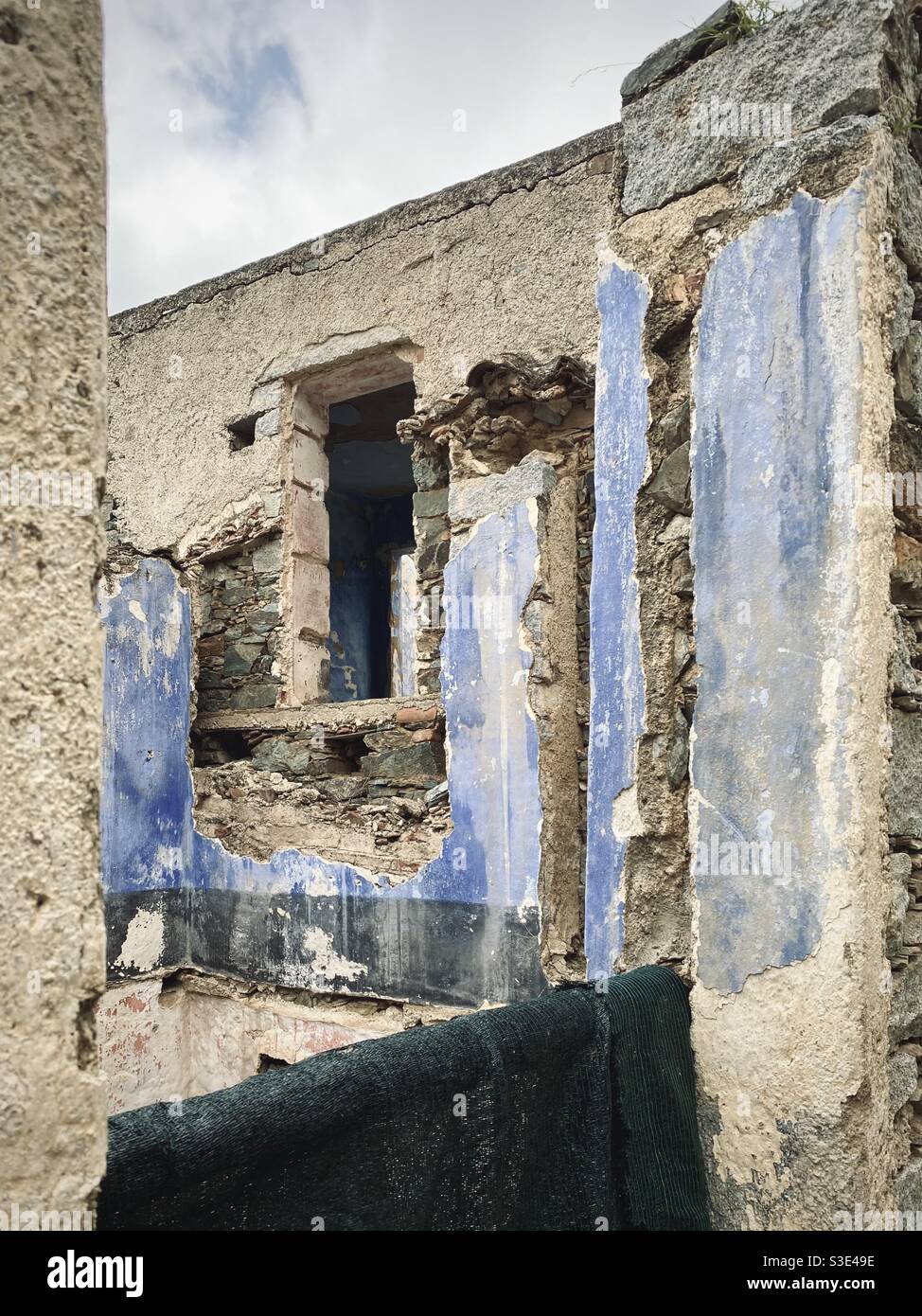 The old ruins of an abandoned and dismissed building in which the blue paint of the internal walls is still visible. Stock Photo