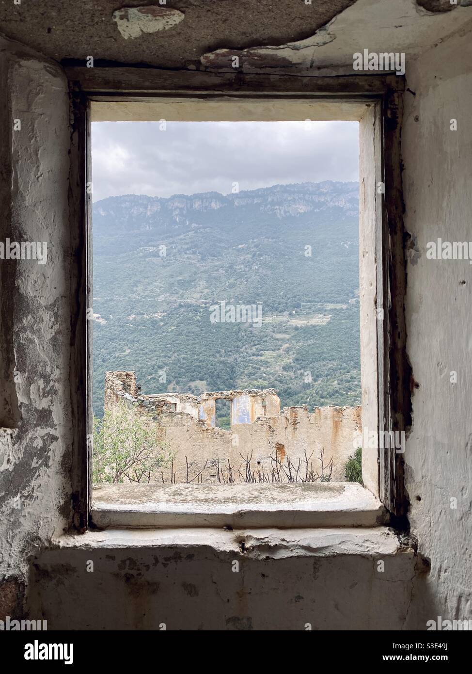 Panoramic view of an abandoned building and green mountains, known as “tacchi”, in the background, from a window of a dismissed and abandoned house of Gairo vecchio ghost town, in Sardinia, Italy. Stock Photo