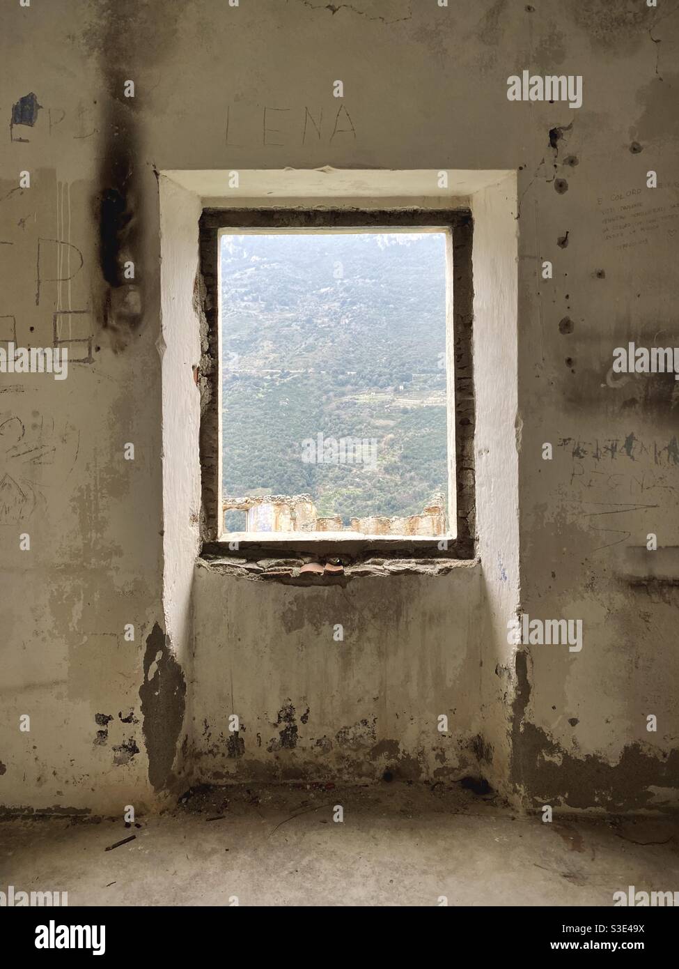 Panoramic view of an abandoned building and green mountains (known as “tacchi”) in the background, from a window of a dismissed and abandoned house of Gairo vecchio ghost town, in Sardinia, Italy. Stock Photo