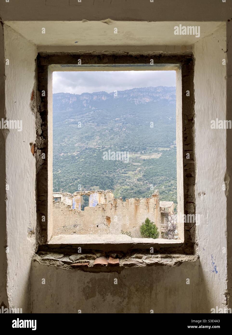 Panoramic view of an abandoned building and green mountains (known as “tacchi”) in the background, from a window of a dismissed and abandoned house of Gairo vecchio ghost town, in Sardinia, Italy. Stock Photo