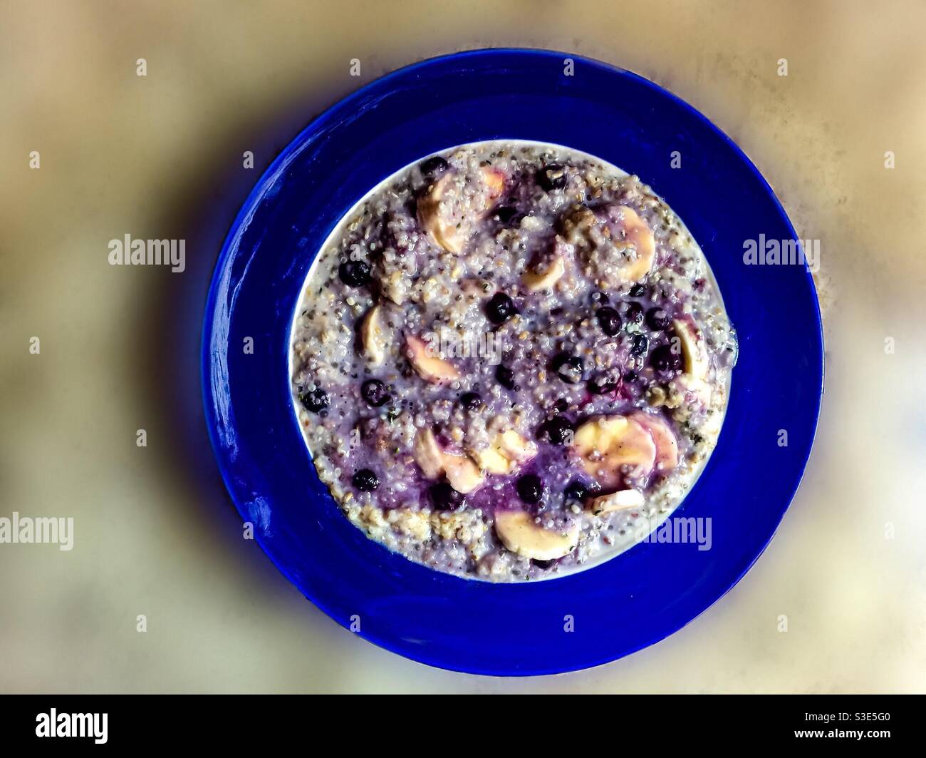 Porridge with banana and blueberries on a soft, out of focus, backdrop. Round bowl with a shiny blue rim. - Smartphone Captured Stock Image