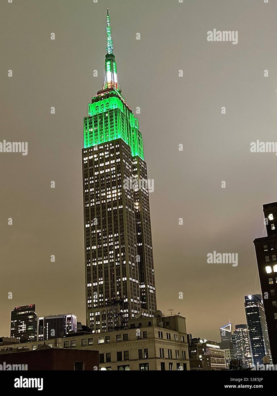 Night view of the Empire State building lit up with green lights for St. Patrick’s Day with the edge at Hudson yards in the background - Smartphone Captured Stock Image