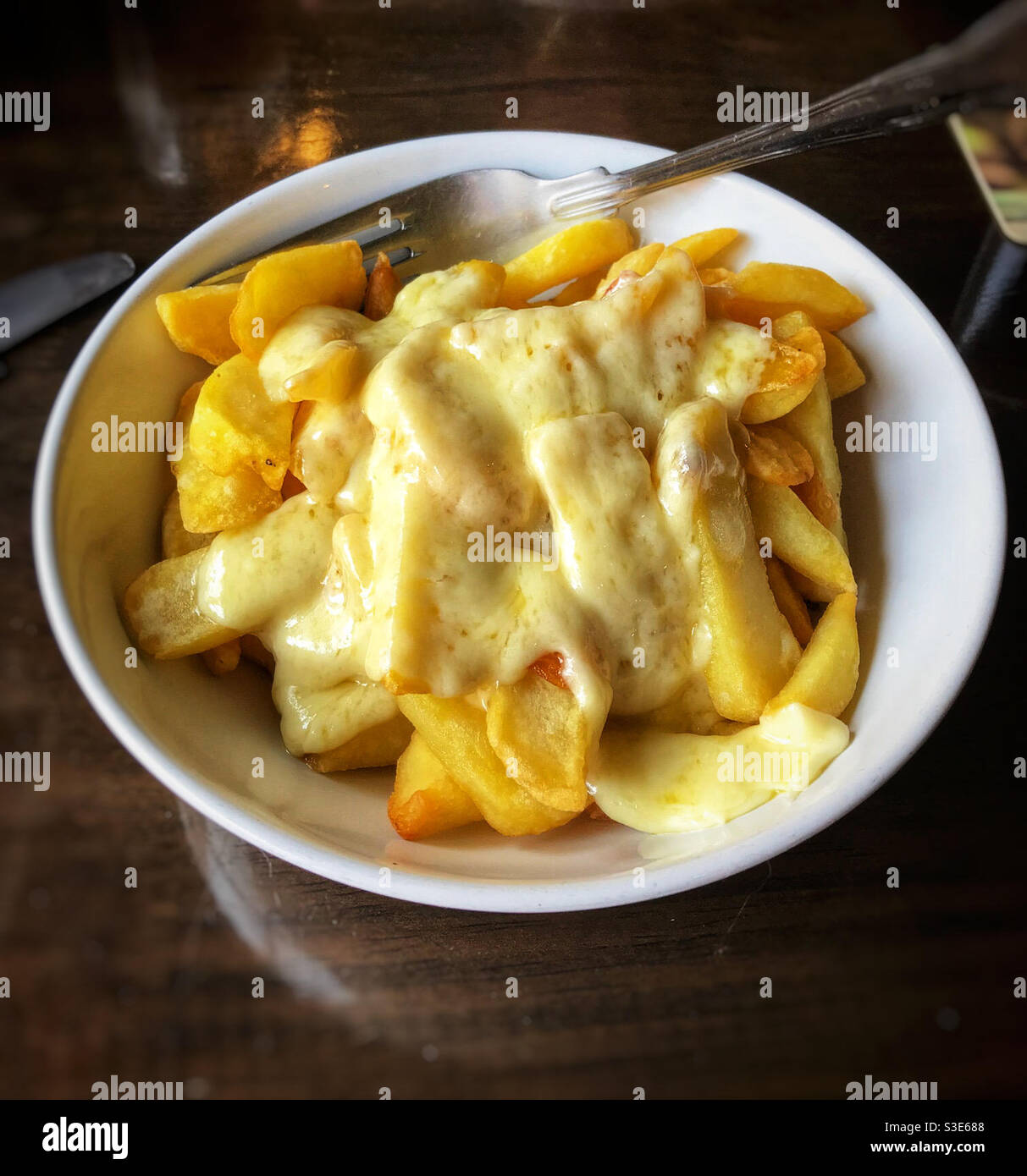 A bowl of cheesy chips. Typical British comfort food and pub snack. - Smartphone Captured Stock Image