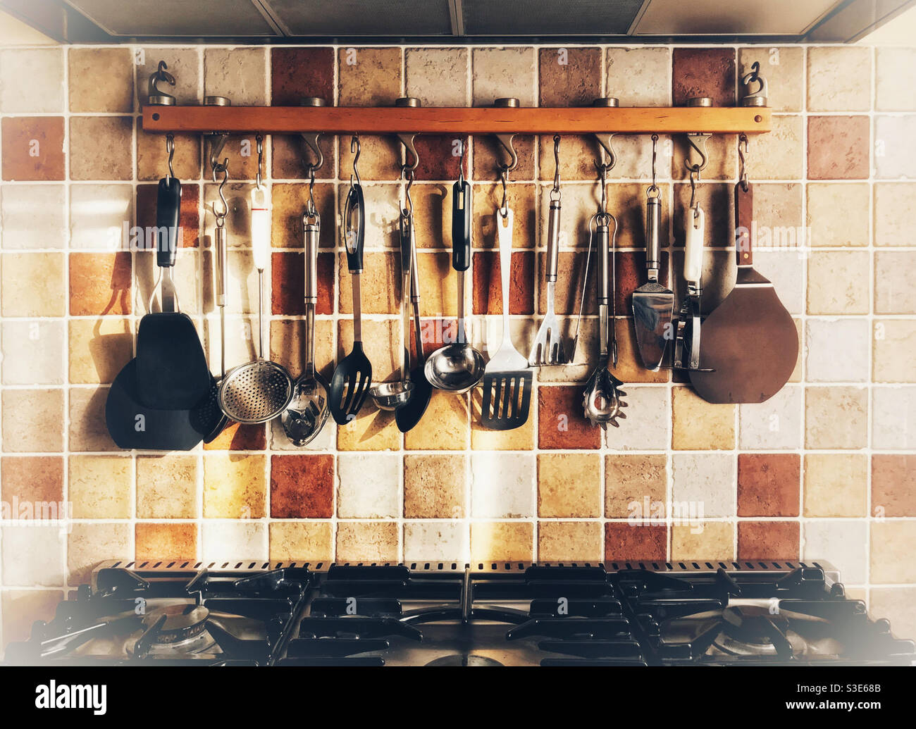 Country-style kitchen with large range cooker top and rack of utensils. Stock Photo