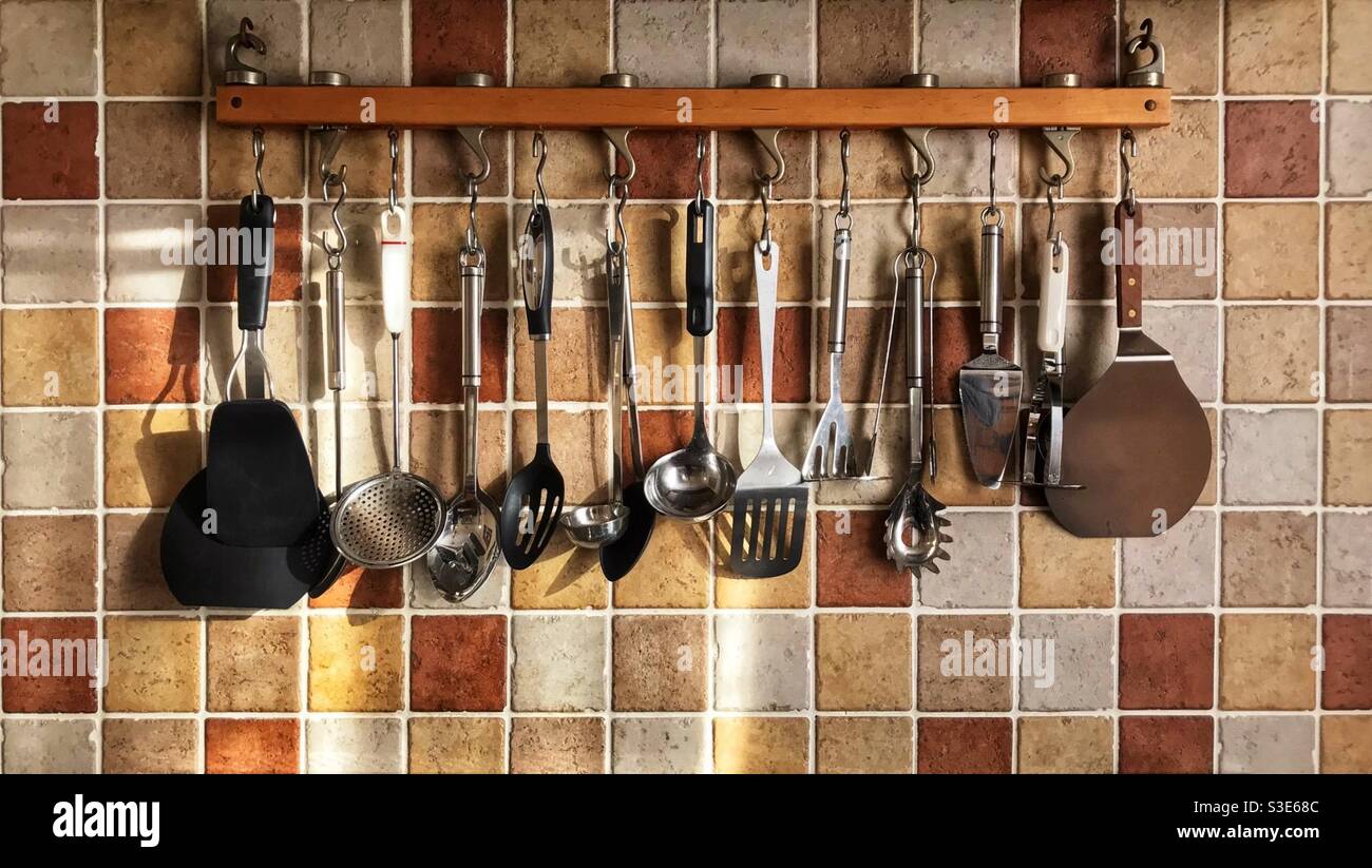 Rack of hanging kitchen utensils against a terracotta tiled wall. Stock Photo