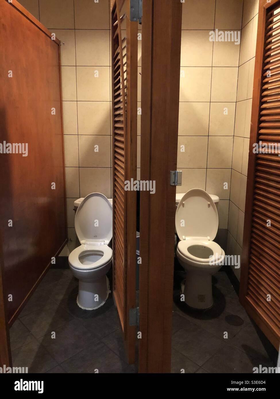 Two toilets in toilet stalls with open doors at a restaurant Stock Photo