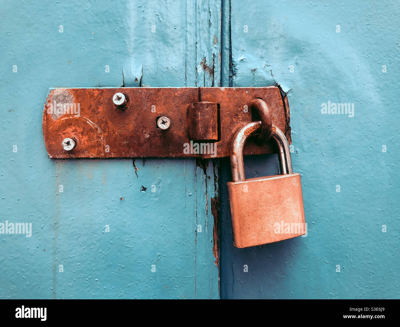 Door closed with a padlock on an led, rusty latch. Stock Photo
