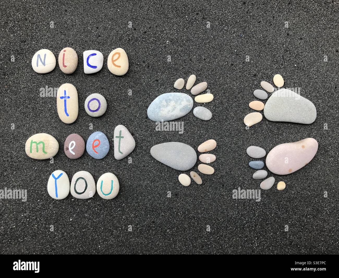 Nice to meet you, creative composition with stone feet and stone carved letters over black volcanic sand - Smartphone Captured Stock Image