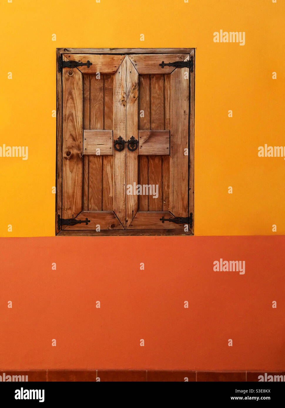 Wooden shutters, with ornate ironwork, block out the hot sunlight, whilst adding an interesting feature to a colourful wall. Jamaica. - Smartphone Captured Stock Image