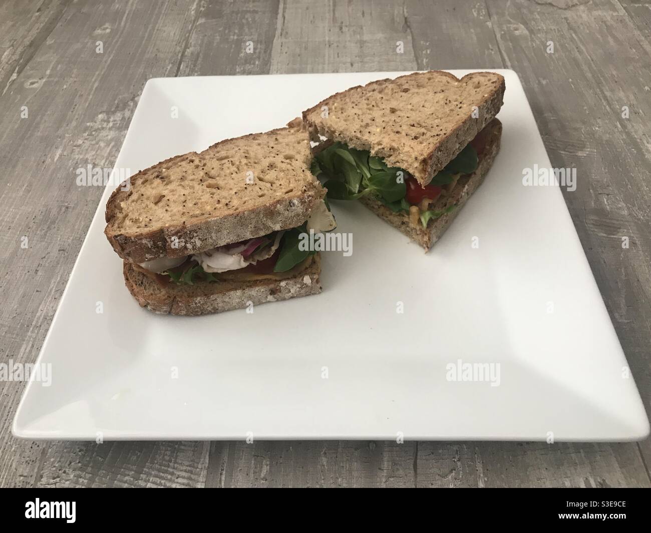 Seeded bread sandwich of crispy bacon, lettuce and tomato on a white plate - Smartphone Captured Stock Image