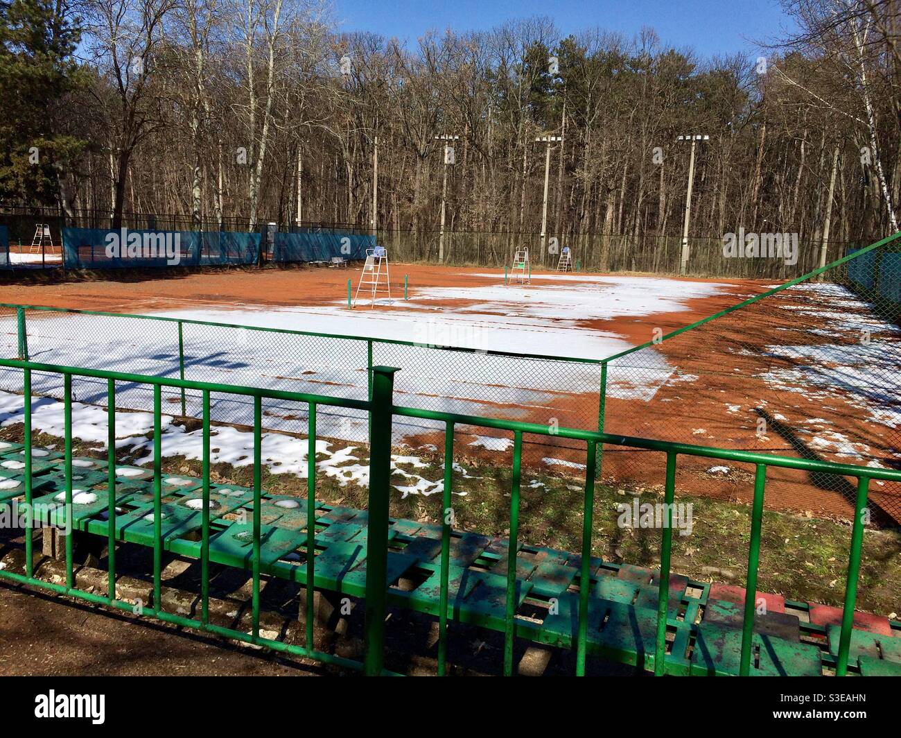 Patches of snow on public clay tennis court in park in Sofia, Bulgaria, Europe - Smartphone Captured Stock Image