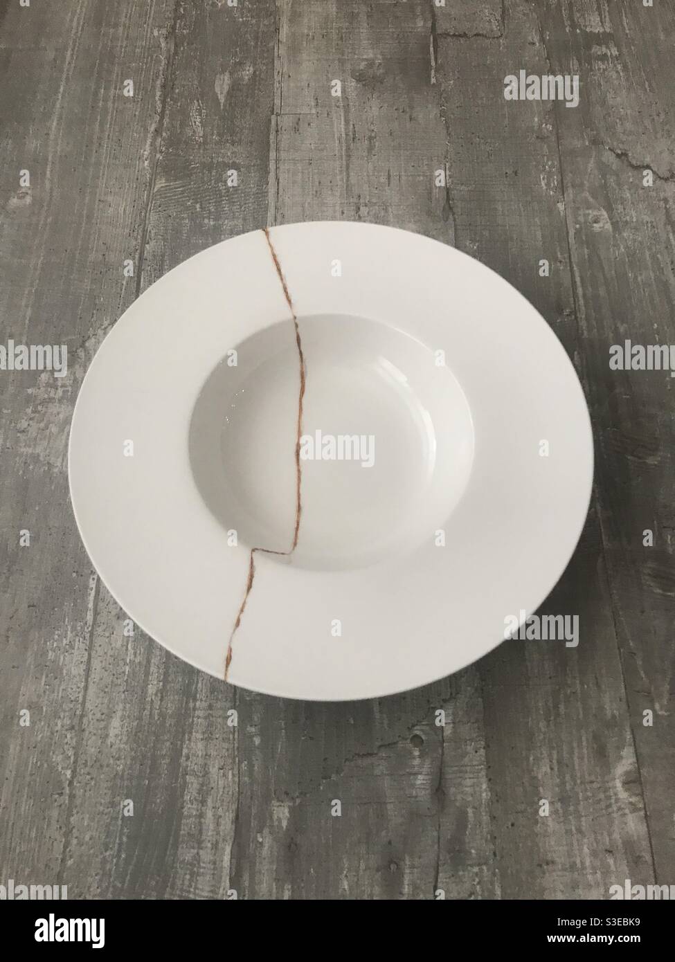 A cracked white bowl repaired using gold powder following the Japanese art of kintsugi - Smartphone Captured Stock Image