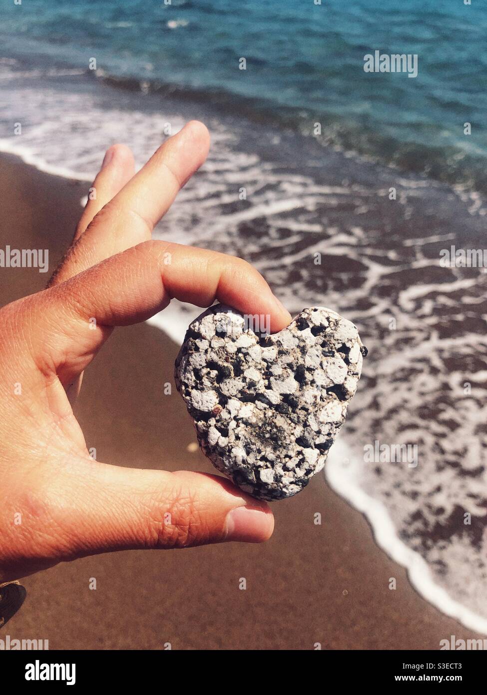 Heart shaped rock held in hand by the sea - Smartphone Captured Stock Image