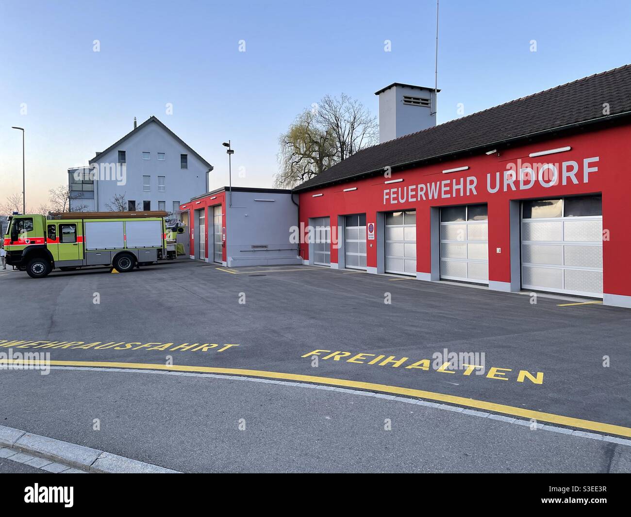 Fire station in Switzerland village Urdorf painted red with fire track outside of garage under blue sky late afternoon. Stock Photo