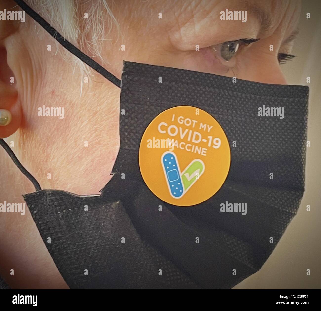 Close up of a senior woman wearing a face mask with a proof of vaccination sticker, USA 2021 - Smartphone Captured Stock Image