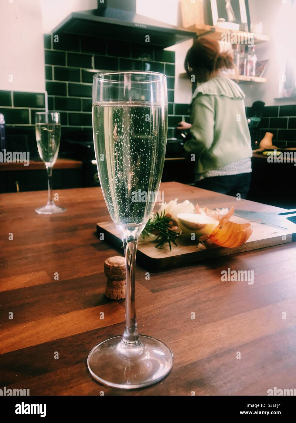 Glass of Prosecco in kitchen with woman cooking in background - Smartphone Captured Stock Image