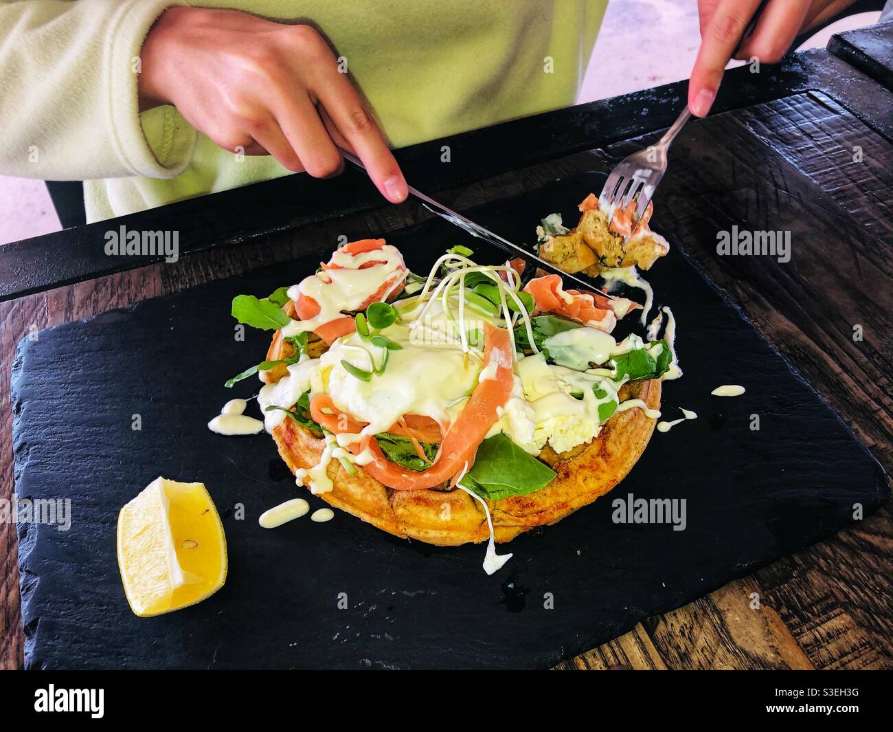 Person eating salmon and poached egg breakfast on a waffle served on a black slate plate Stock Photo
