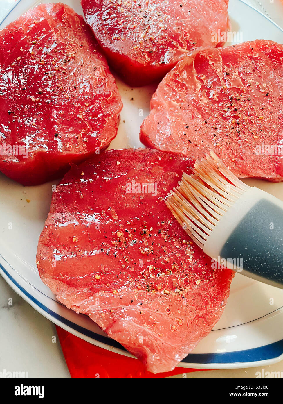 Raw tuna steaks being prepared for grilling with a basting brush - Smartphone Captured Stock Image