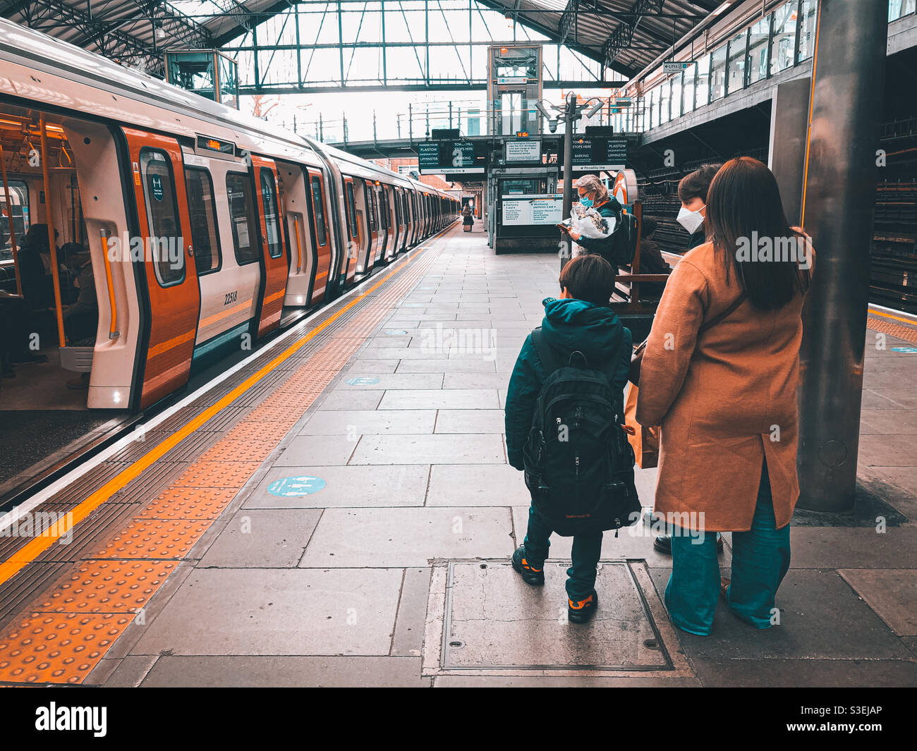 A family wait for a train on the platform at Earl’s Court London Underground Station. They wear face masks because of coronavirus. - Smartphone Captured Stock Image
