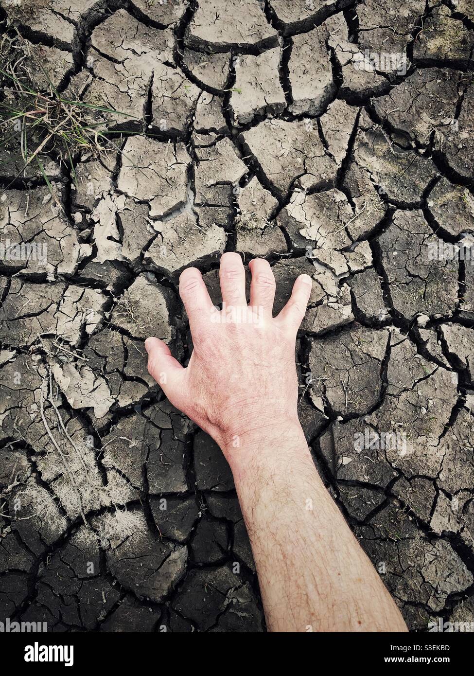 Human hand digging clawing and scratching at a cracked and dried up earth in a drought concept - Smartphone Captured Stock Image