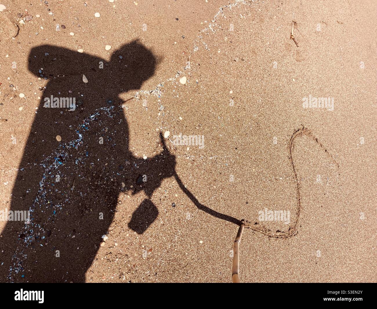 Shadow of man drawing sand with stick - Smartphone Captured Stock Image