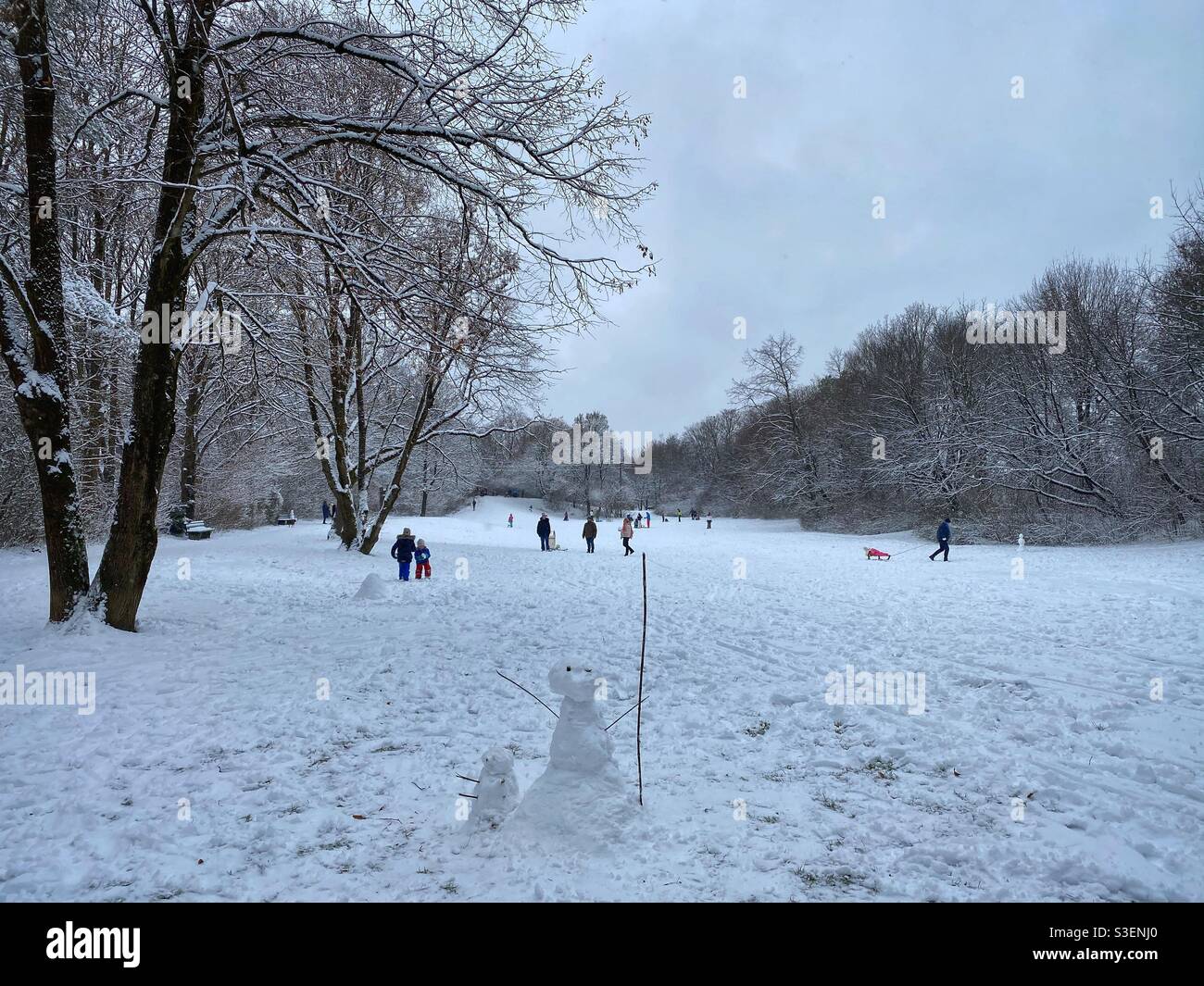 Snowman with sledding people and kids in the background in Fideliopark, Munich, Germany. - Smartphone Captured Stock Image