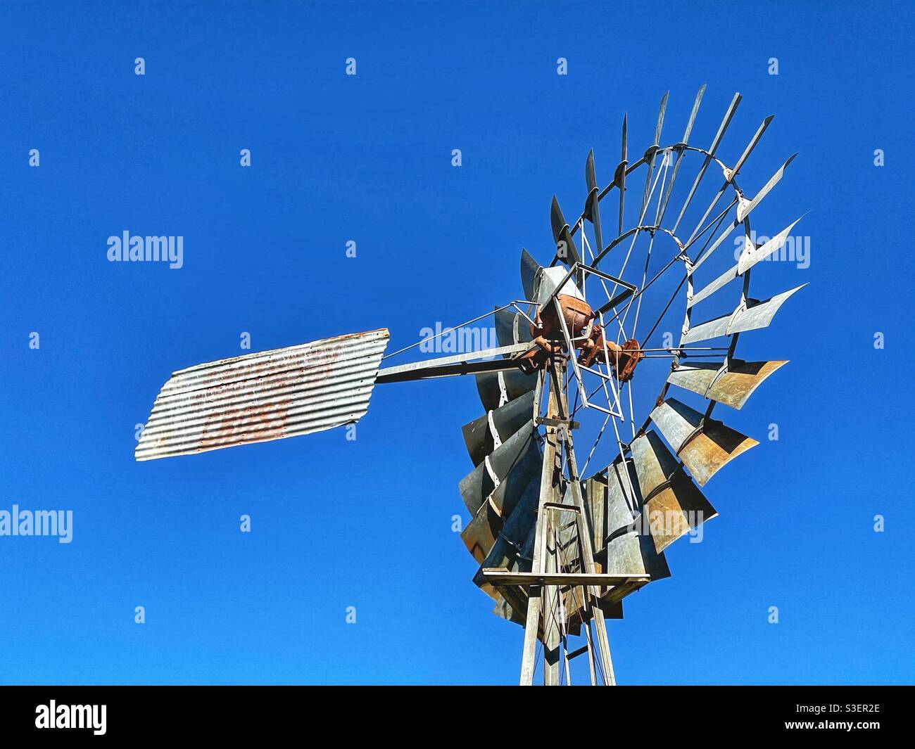 Historic metal windmill against clear blue sky at the Pioneer Village in Inverell, New South Wales, Australia - Smartphone Captured Stock Image