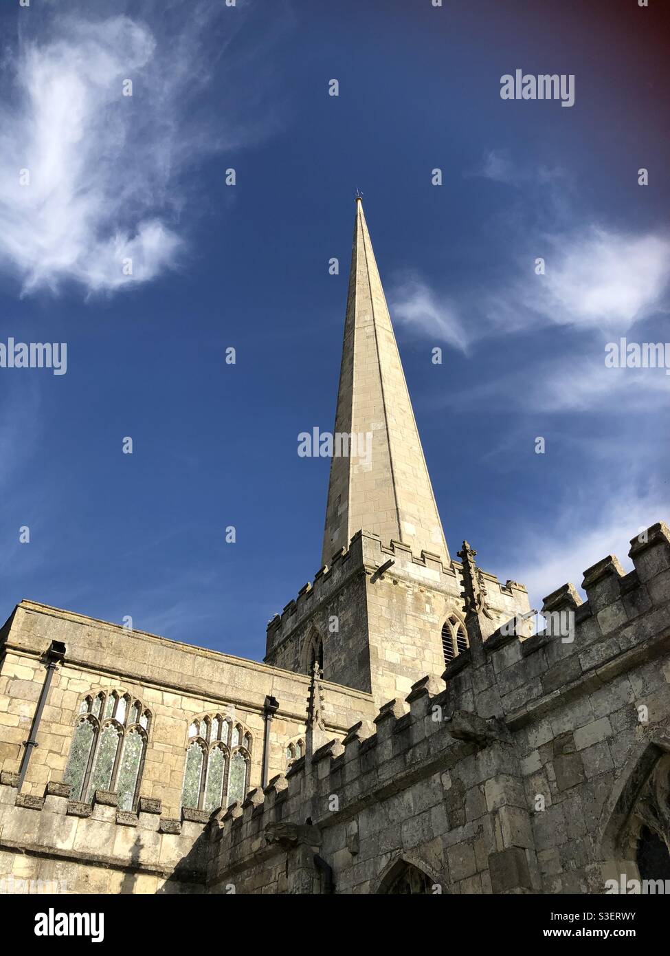 Looking up to a beautiful sunny and intense blue spring sky framed by a lofty church spire and church buildings in Yorkshire. Stock Photo