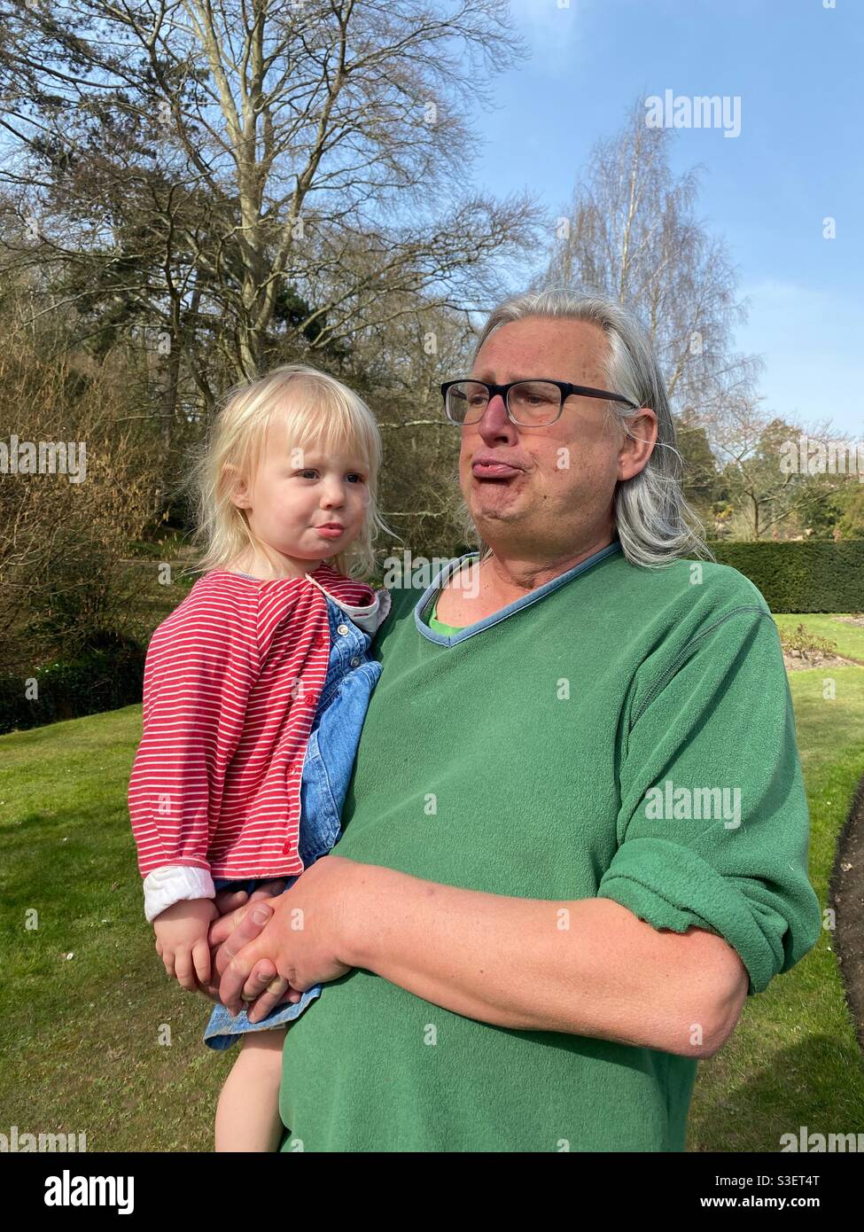 Grandad teaching his granddaughter how to blow raspberries Stock Photo