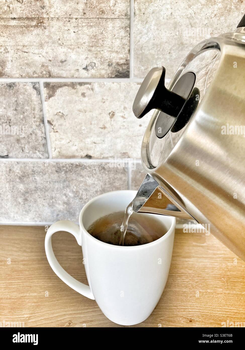 Pouring hot water into a white mug from the kettle- Making a cup of tea in the kitchen Stock Photo