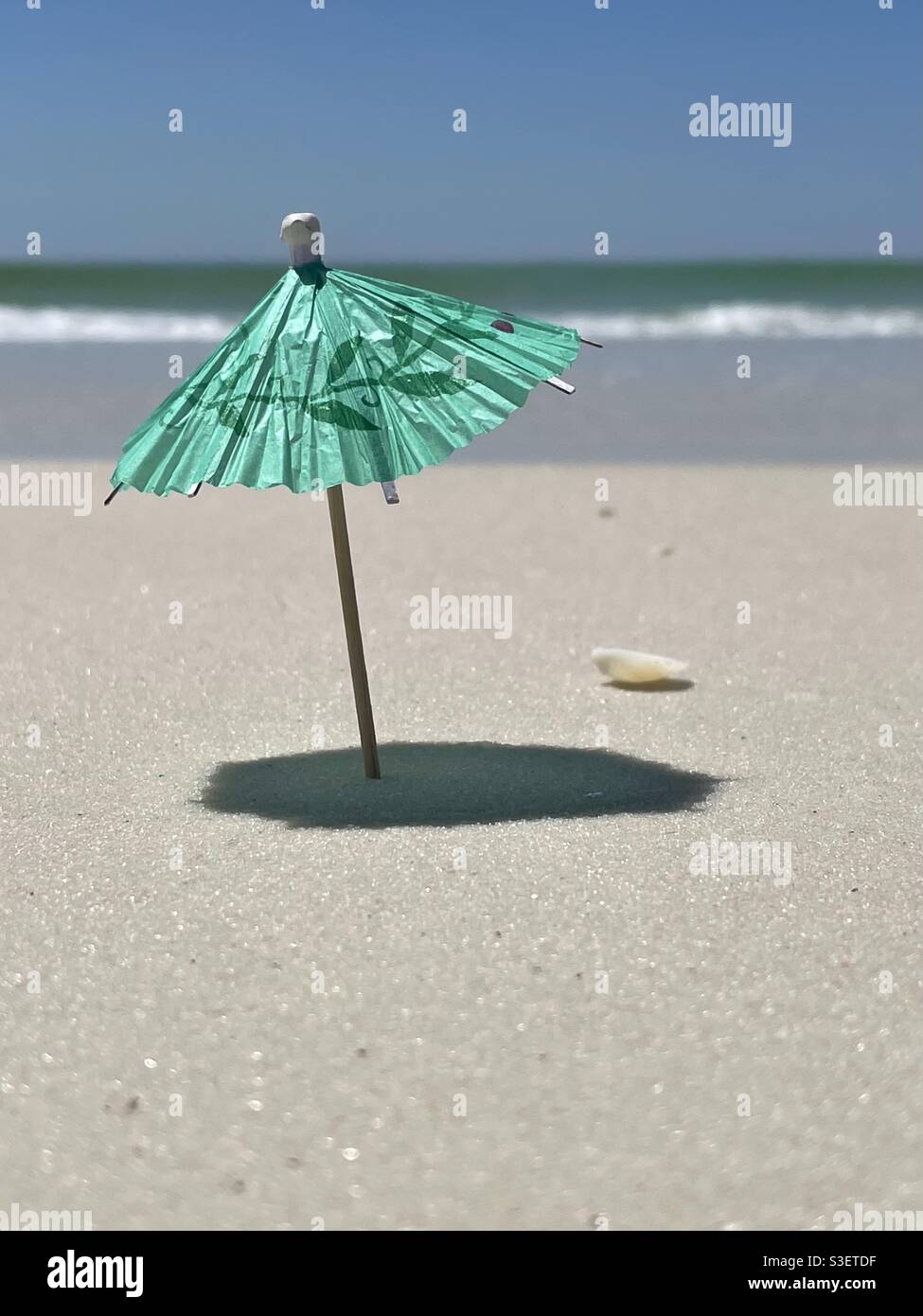 Select focus on miniature green umbrella with blurred beach background Stock Photo