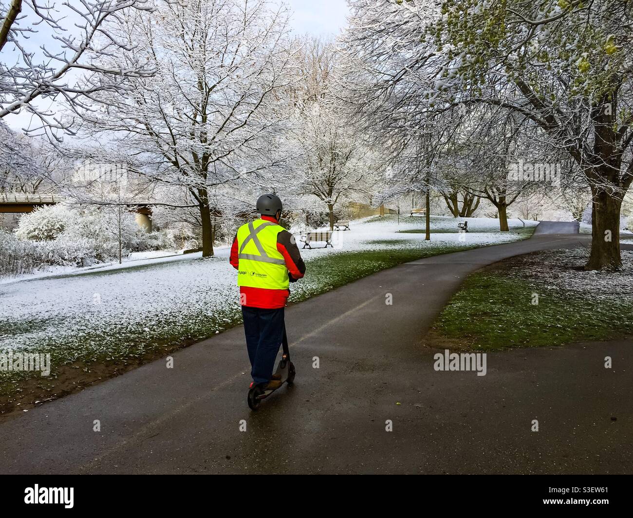 A man on a power scooter in a park in snow, Ontario, Canada. Concepts: winter, fun, outing,solo, unusual, balance. Spring and winter, equal parts. Seasons blending, overlapping, stitched together. - Smartphone Captured Stock Image