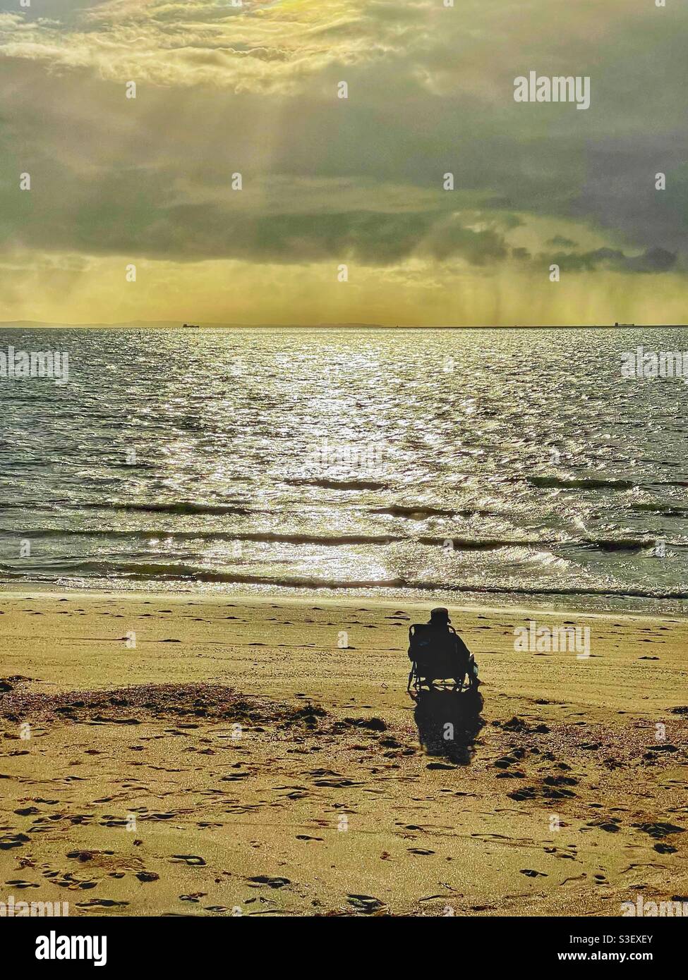 One person sitting on a beach in the early morning sunlight, Margate, Queensland, Australia - Smartphone Captured Stock Image
