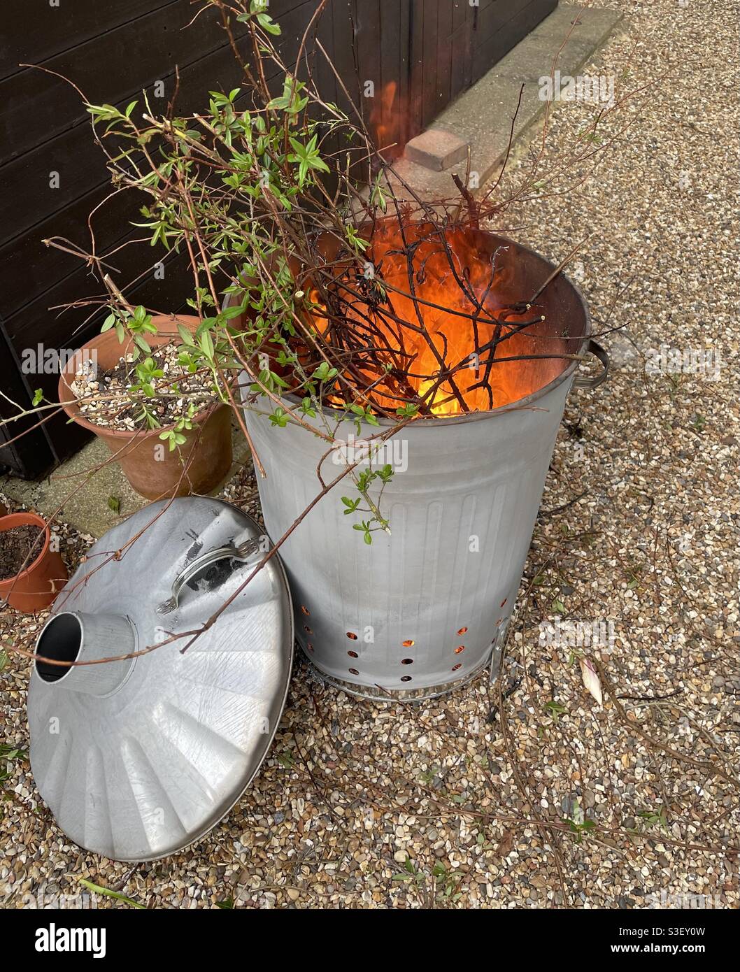 Wood and twigs burning in metal incinerator on gravel floor - Smartphone Captured Stock Image