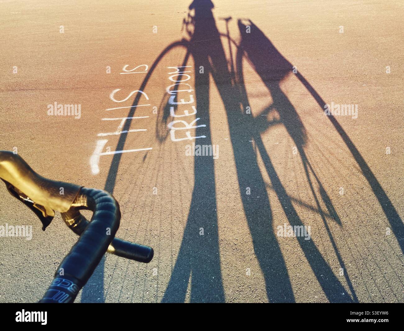 A shadow of a Bicycle with the words this is Freedom written as a Graffiti in the Pavement on Tempelhofer Feld, Berlin, Germany - Smartphone Captured Stock Image