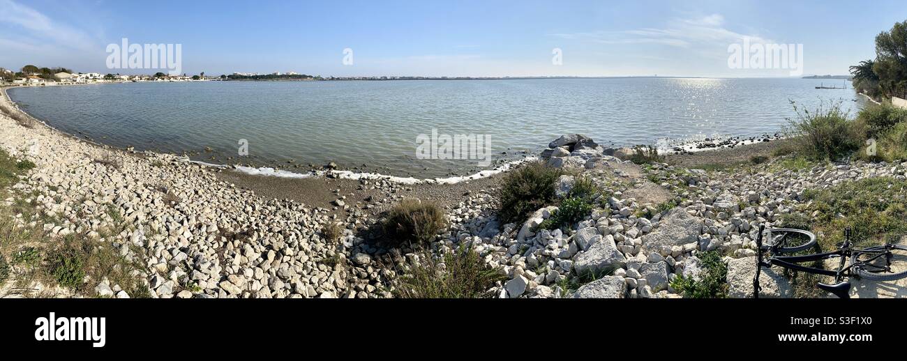 Panorama of a salt lake with a rocky beach in the south of France, black bicycle - Smartphone Captured Stock Image