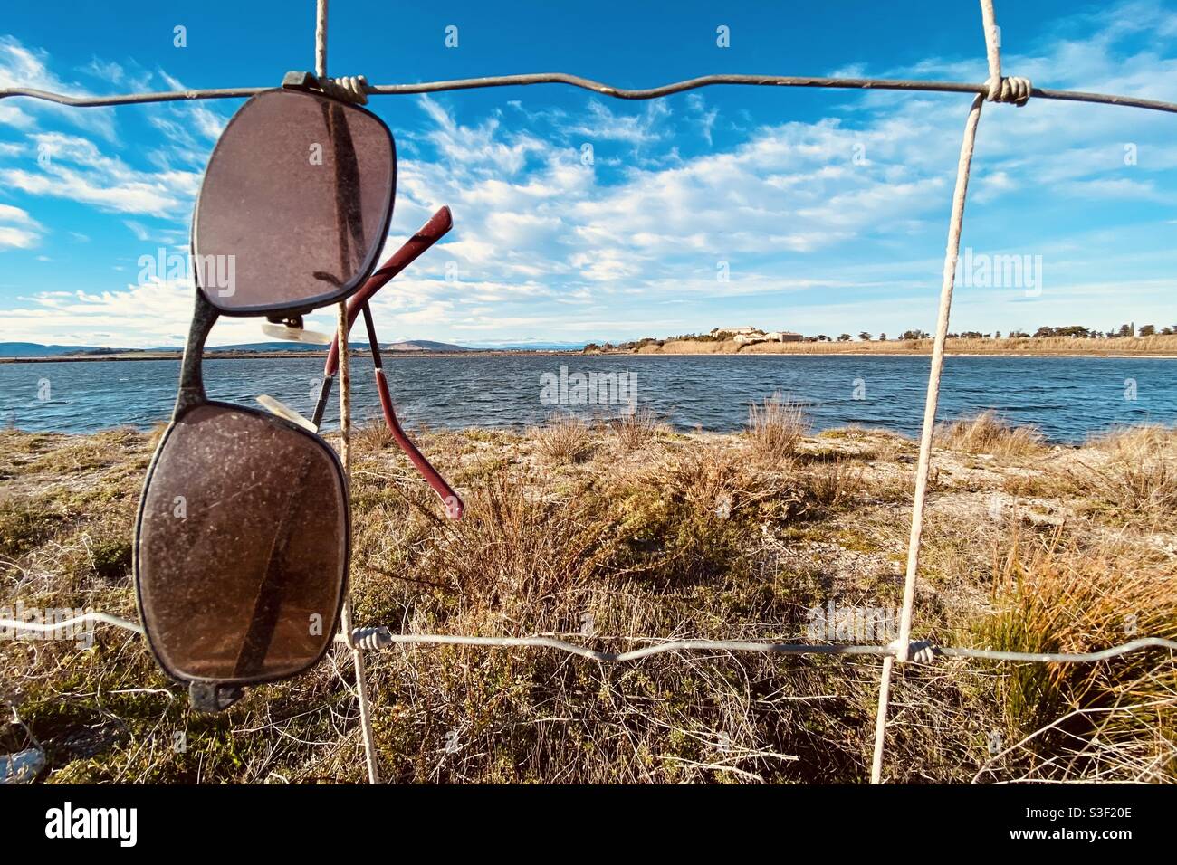 Beautiful landscape of a salt lake against blue cloudy sky, with a pair of sunglasses attached to a steel fence - Smartphone Captured Stock Image