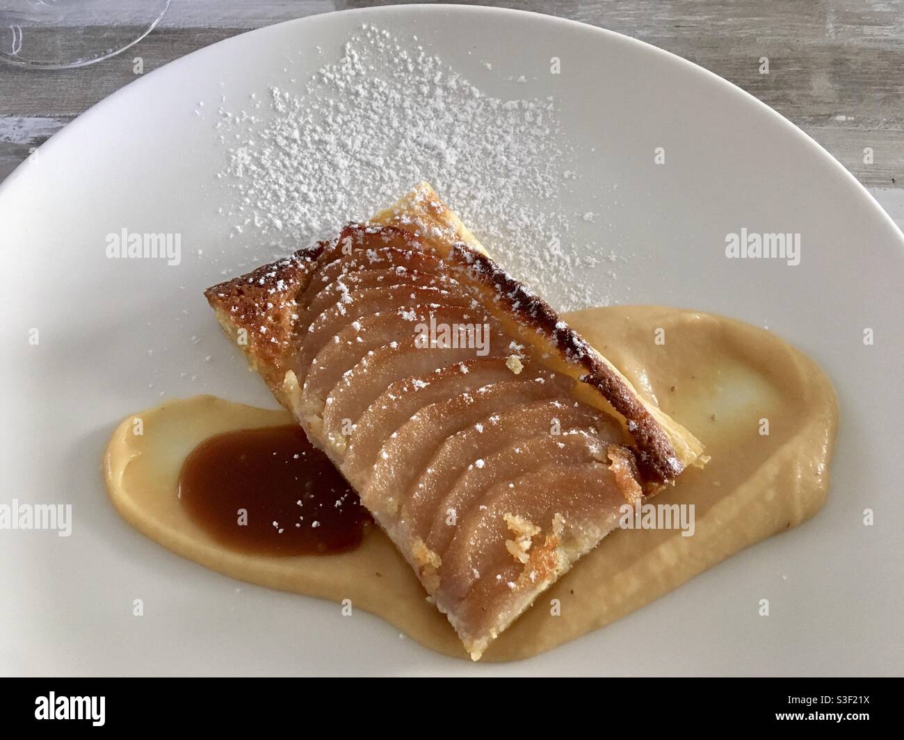 Pear or apple pie slice on apple sauce and salted caramel dessert on white restaurant dish plate - Smartphone Captured Stock Image