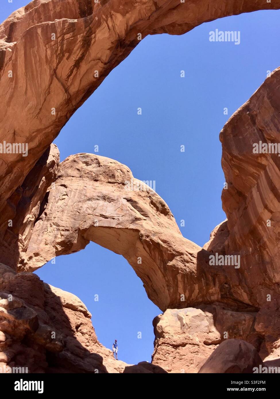 A visitor is dwarfed by the massive Double Arch formation in Arches National Park, Utah - Smartphone Captured Stock Image