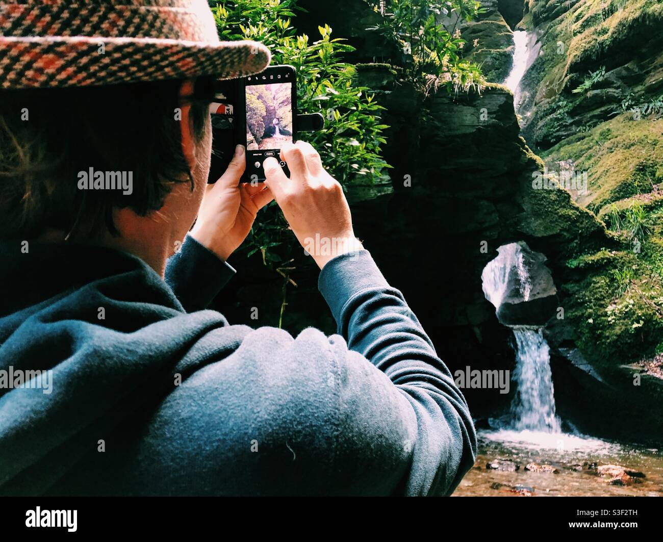 Man taking a photo on his phone at Nectan’s glen waterfall in Cornwall - Smartphone Captured Stock Image