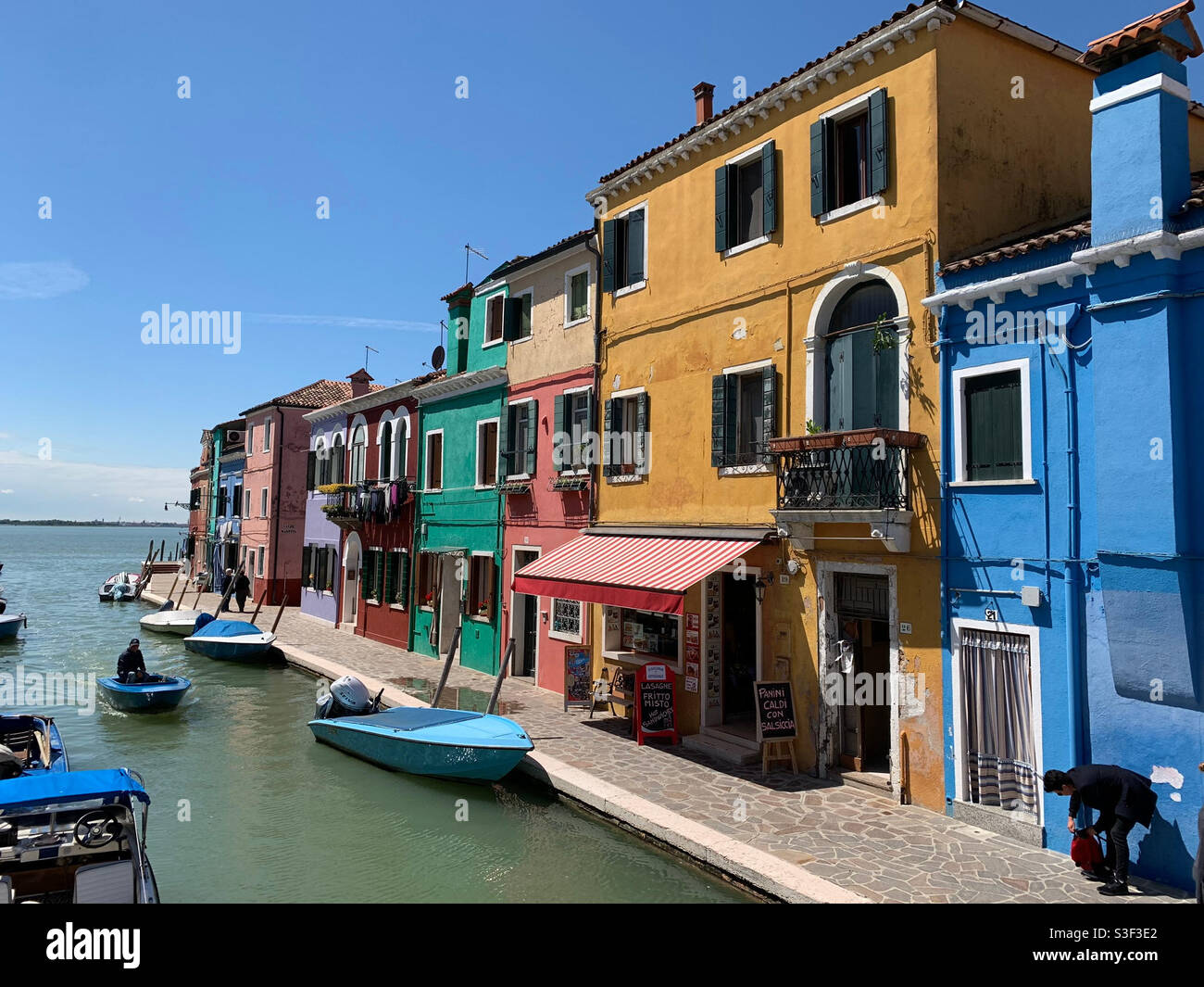 Coloured shops in Burano Italy, facing the sea with Venice on the horizon. - Smartphone Captured Stock Image